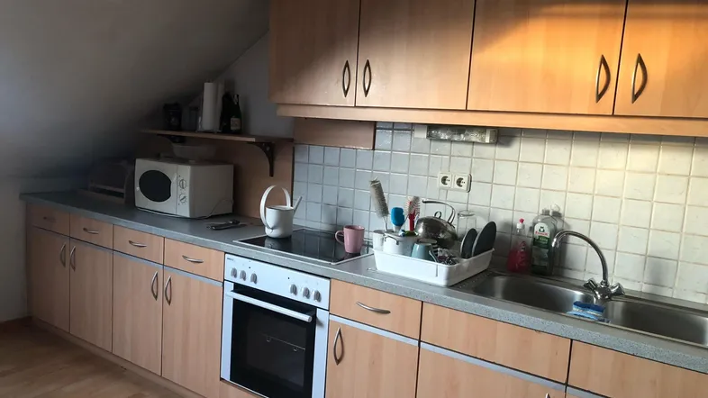 Funktionale Küche im Dachgeschoss mit hellen Holzschränken, Einbauherd und Spüle unter der Dachschräge.