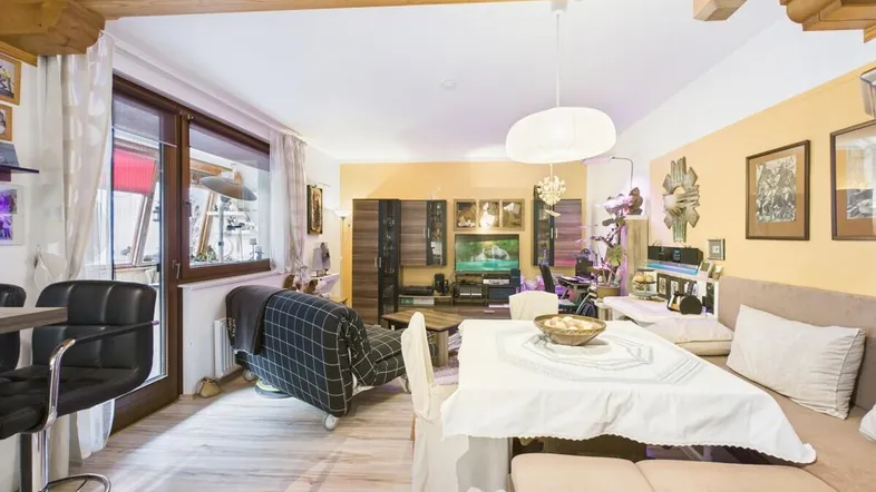 Geräumiger Wohn-Essbereich mit Holzbalkendecke, Parkettboden und Zugang zu einem Balkon.