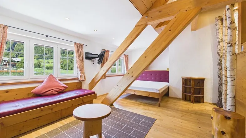Helles Schlafzimmer im Dachgeschoss mit Holzbalken, gemütlicher Sitzecke und Blick ins Grüne.
