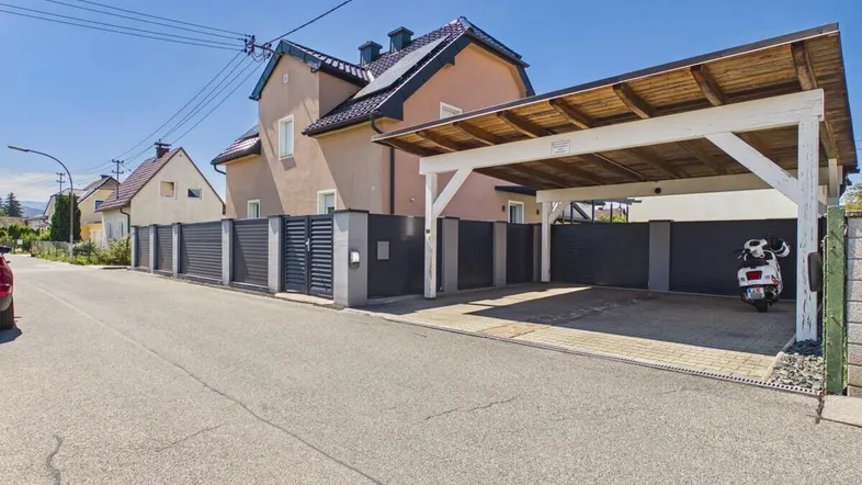 Vorderansicht des Hauses mit modernem Zaun, Carport und Zufahrt von der Straße.