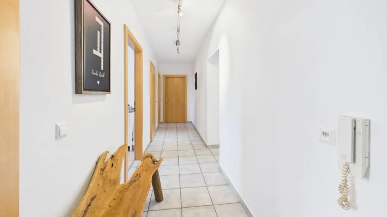 Heller Flur mit Fliesenboden, Holztüren und moderner Deckenbeleuchtung.