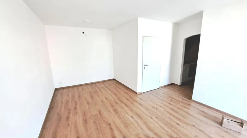 Helles, leeres Zimmer mit Laminatboden und weiß gestrichenen Wänden, bereit zur individuellen Gestaltung.