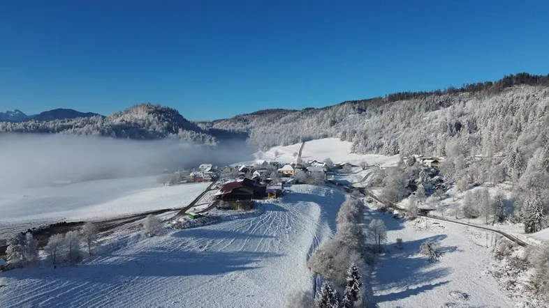 Winterliche Luftaufnahme eines verschneiten Dorfes in einer bergigen Landschaft mit Nebel.