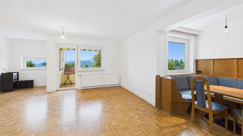 Heller Wohn- und Essbereich mit Parkettboden, großen Fenstern und Zugang zum Balkon.