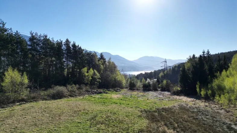 Weitläufiger Blick über grüne Hügel und Wälder auf einen See und die umliegende Berglandschaft.