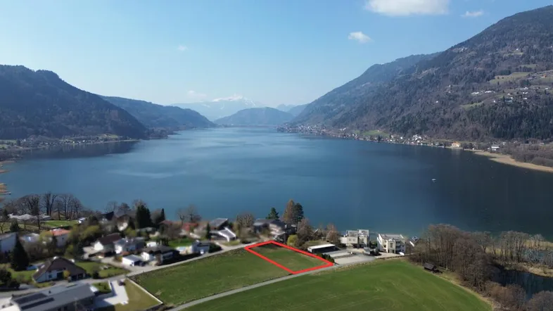 Luftaufnahme eines Grundstücks am See mit umliegender Berglandschaft und klarem Himmel.