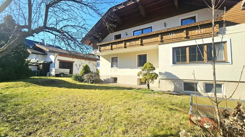 Seitenansicht des Hauses mit gepflegtem Rasen und Sträuchern unter blauem Himmel.