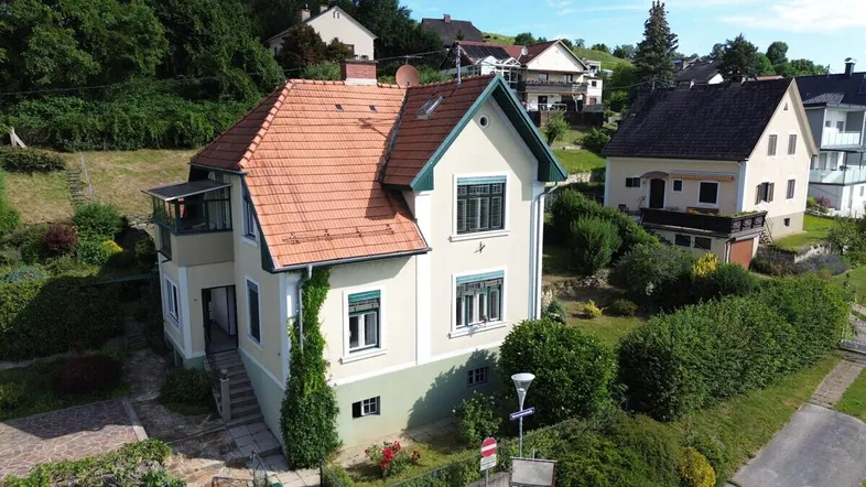 Charmantes Haus mit traditionellem Ziegeldach und grüner Umgebung am Hang.