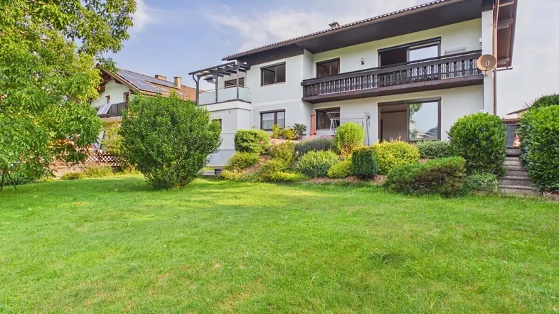 Großzügiger Gartenbereich mit gepflegtem Rasen und Blick auf das Wohnhaus mit Balkonen.