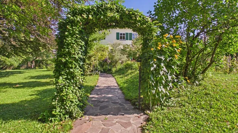 Idyllischer Gartenweg mit bewachsenem Torbogen, der zum Haus führt.
