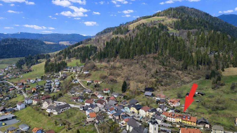 Luftaufnahme eines malerischen Dorfes in den Bergen mit grünen Hügeln und blauem Himmel.