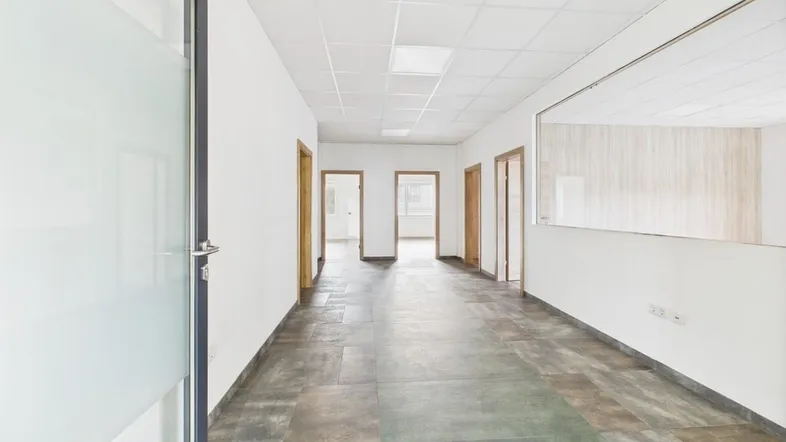 Langer Flur in einem Bürogebäude mit mehreren Türen und Fliesenboden.