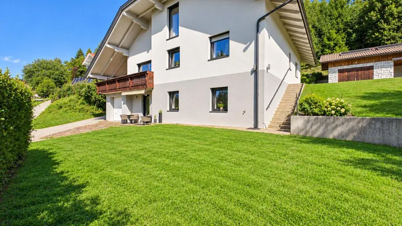Modernes Einfamilienhaus mit gepflegtem Rasen, Balkon und kleiner Terrasse im Grünen.