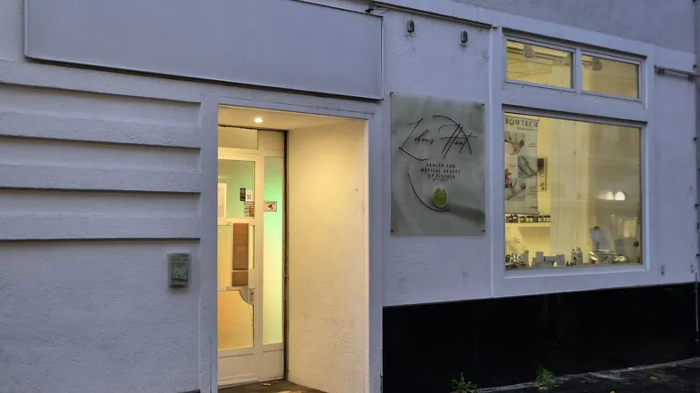 Fassade eines Geschäftsgebäudes mit Eingangstür und großen Schaufenstern, die auf eine Straße blicken.