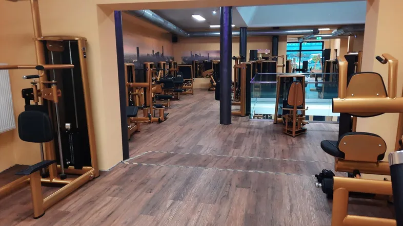 Geräumiger Fitnessraum mit zahlreichen Trainingsgeräten, Holzbodenoptik und orangefarbenen Wänden.