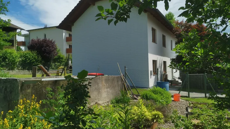 Ansicht des Hauses von der Gartenseite mit üppiger Bepflanzung und einem kleinen Spielbereich.