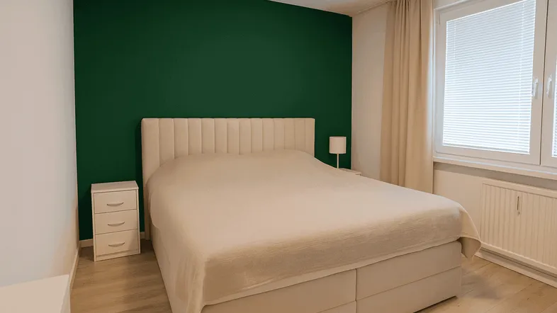 Schlafzimmer mit großem Doppelbett, Nachttischen und einer auffälligen grünen Akzentwand.