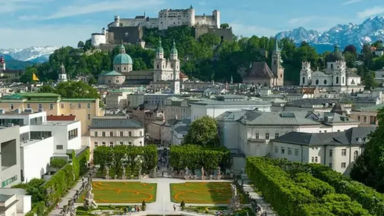 Panoramablick auf die historische Stadt Salzburg mit der Festung Hohensalzburg und gepflegten Gärten im Vordergrund.