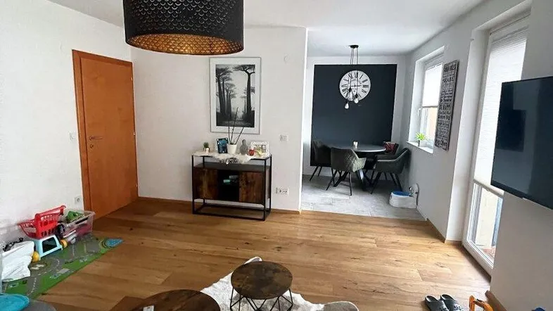 Geräumiger Wohnbereich mit Holzboden, gemütlichem Sofa und offenem Übergang zum Essbereich mit dunkler Akzentwand.