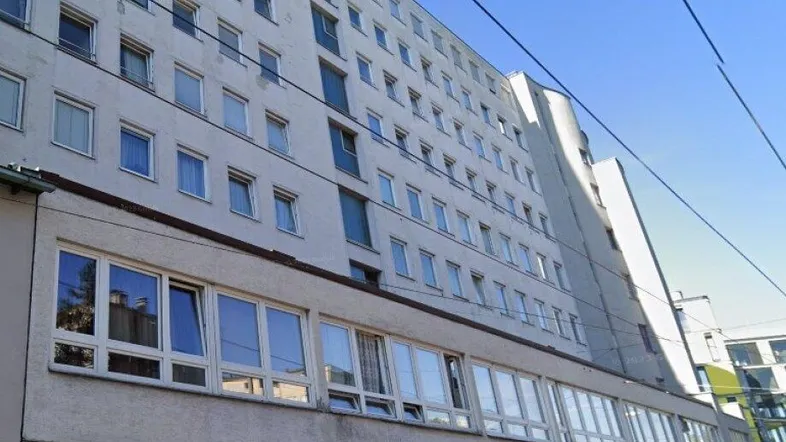 Mehrstöckiges Wohngebäude mit zahlreichen Fenstern und Geschäften im Erdgeschoss unter blauem Himmel.