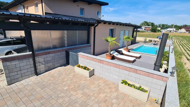 Ansicht des Hauses mit Carport, Poolbereich und Liegestühlen, umgeben von Feldern.