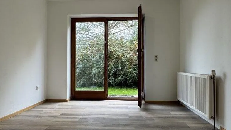 Helles Zimmer mit Holzboden und großer Glastür, die direkten Zugang zum Garten bietet.