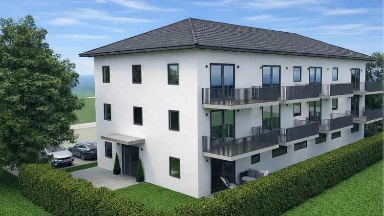 Modernes Mehrfamilienhaus mit weißer Fassade, mehreren Balkonen und Blick auf die Landschaft.