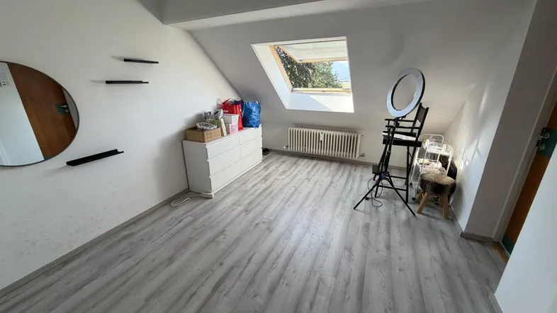 Helles Dachzimmer mit Schrägdach, Dachfenster und modernem Laminatboden.