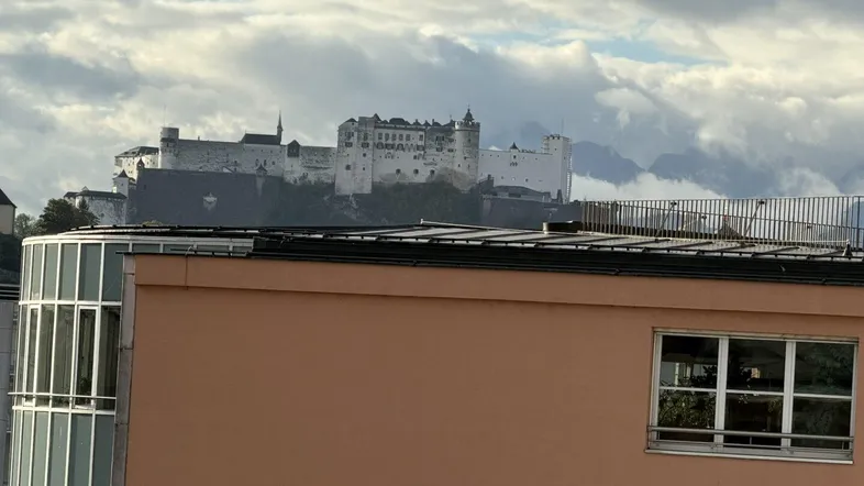 Blick auf die Festung Hohensalzburg über den Dächern der Stadt unter bewölktem Himmel.