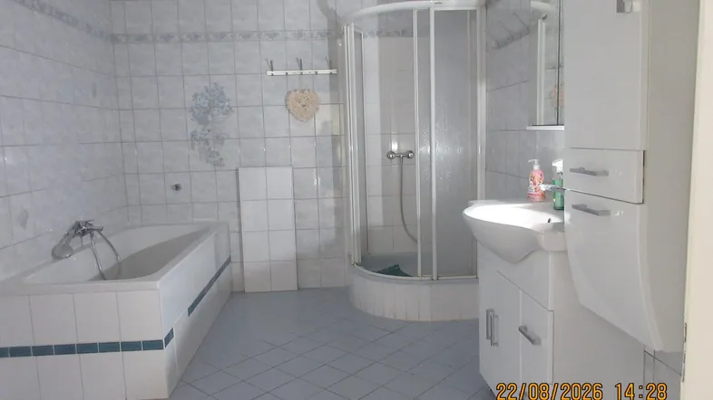 Badezimmer mit Badewanne, Duschkabine, Waschbecken und Spiegelschrank in hellblauen Fliesen.