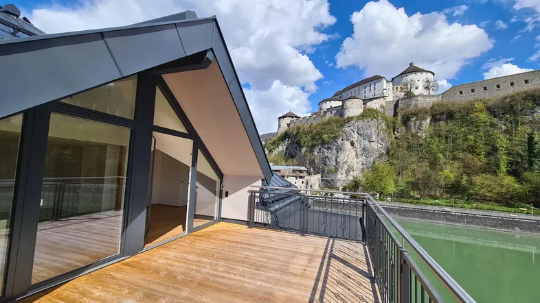 Geräumige Holzterrasse mit Blick auf eine historische Burg und einen Fluss unter blauem Himmel.