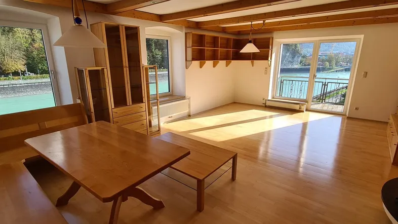 Helles Wohn- und Esszimmer mit Holzbalken, Parkettboden und Zugang zum Balkon mit Flussblick.