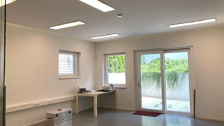 Modernes Büro mit großen Schiebetüren zur Terrasse und viel Tageslicht, ausgestattet mit Einbaulampen.
