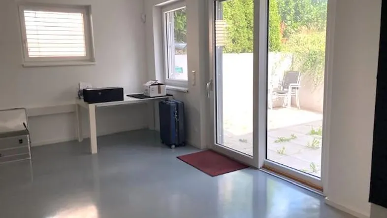 Heller Büroraum mit grauem Boden, großen Fenstern und Zugang zu einer kleinen Terrasse.