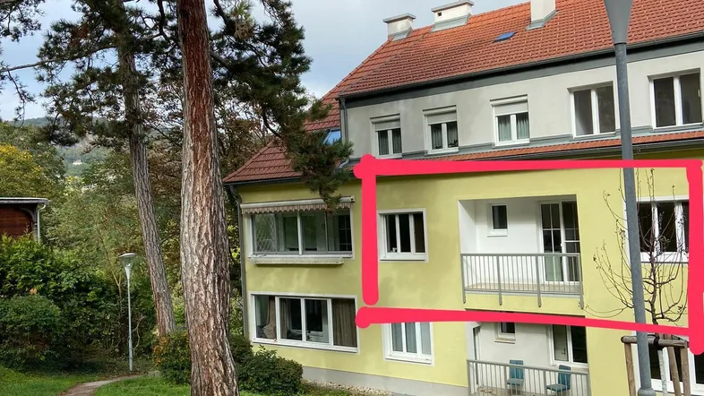 Gelbe Fassade eines Mehrfamilienhauses mit Balkon und grünem Vorgartenbereich.