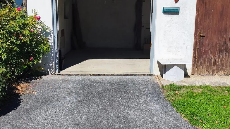 Offene Garage mit Betonboden und asphaltierter Einfahrt, bereit zur Nutzung unter blauem Himmel.