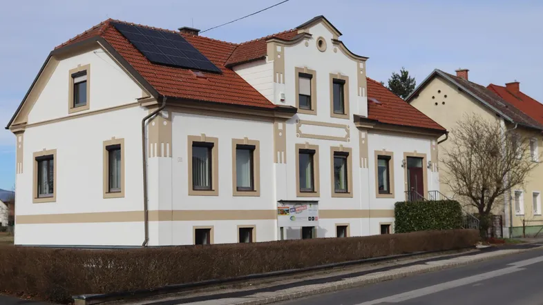 Traditionelles Gebäude mit weißer Fassade, rotem Ziegeldach und modernen Solarpaneelen auf dem Dach.