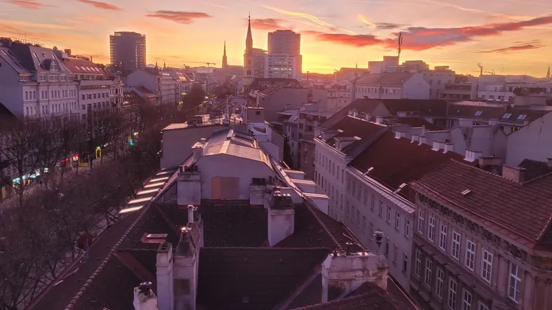 Sonnenuntergang über der Stadt mit Blick auf historische Gebäude und moderne Skyline.