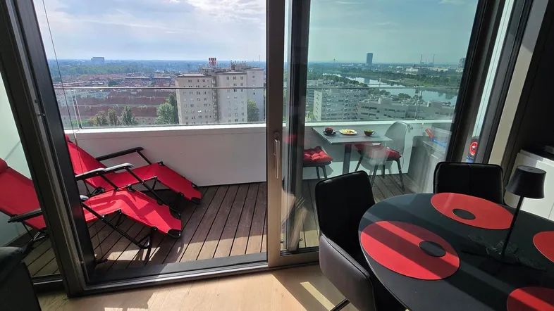 Heller Wohnbereich mit Esstisch, Balkonzugang und weitem Blick über die Stadt und den Fluss.