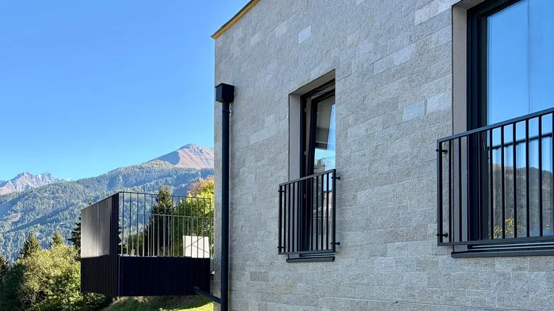 Moderne Fassade mit Steinverkleidung, großen Fenstern und atemberaubendem Bergblick.