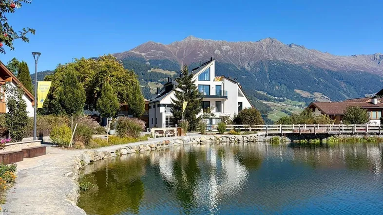 Modernes weißes Gebäude am Seeufer mit Bergblick unter klarem blauem Himmel.