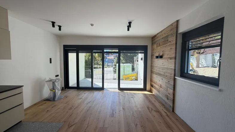 Heller offener Wohnbereich mit Eichenparkett, Holzwand und Zugang zu einem Balkon.