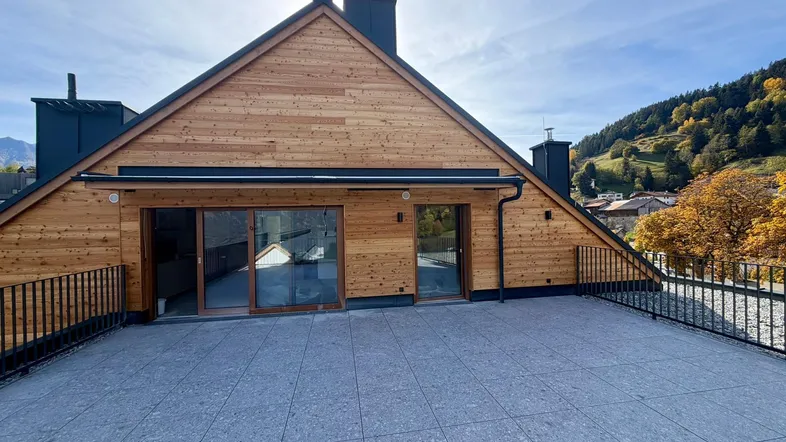 Große geflieste Terrasse mit Holzfassade und weitem Blick auf die umliegende Berglandschaft.