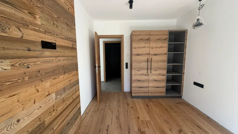 Helles Schlafzimmer mit Holzwandverkleidung, Parkettboden und modernem Kleiderschrank.