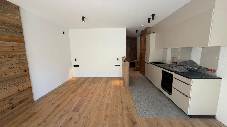 Heller offener Wohnbereich mit Holzboden und integrierter Küchenzeile im Neubau.