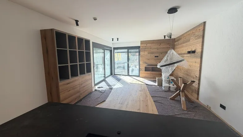 Helles Wohnzimmer im Bau mit Holzwandverkleidung und großen Fenstern, die viel Tageslicht hereinlassen.