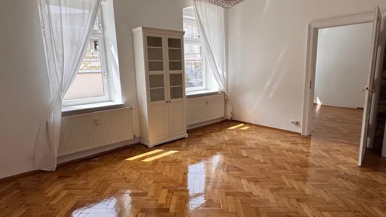 Helles Wohnzimmer mit Fischgrätparkett, hohen Decken und einem eleganten Kronleuchter.