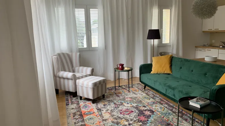 Helles Wohn- und Esszimmer mit gemütlichem Sofa, Sessel und integrierter Küchenzeile.