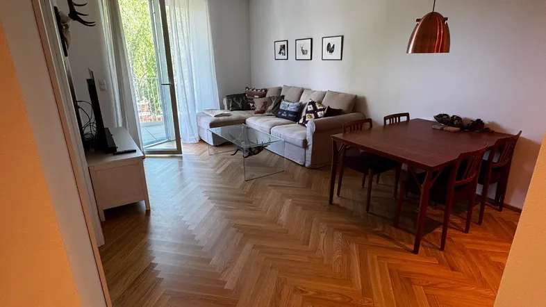 Helles Wohn- und Esszimmer mit Fischgrätparkett, Zugang zum Balkon und moderner Einrichtung.