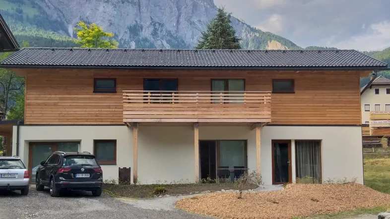 Modernes Gebäude mit Holzfassade, Balkon und beeindruckendem Bergblick in ländlicher Umgebung.